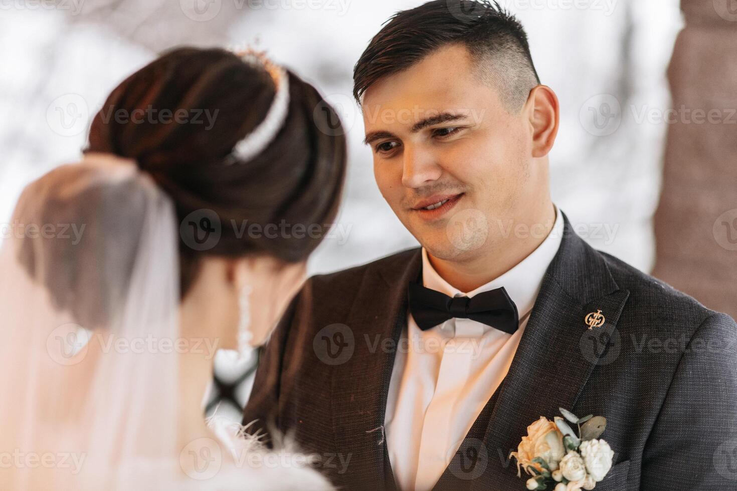 Beautiful wedding couple. Winter wedding of the groom in a beautiful suit and the bride in a beautiful wedding dress. Winter photo session of newlyweds. Gentle look of the groom at the bride