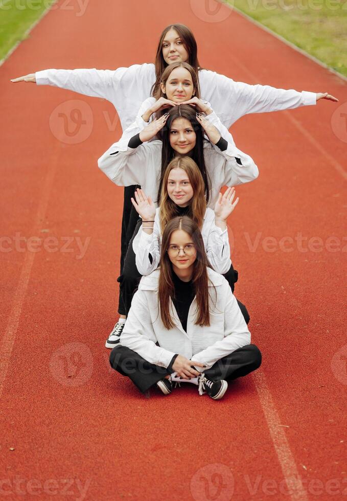 A group of smiling and happy teenage friends, dressed in casual clothes, spend time together, pose and have fun on the grounds of an educational institution on an autumn day. photo