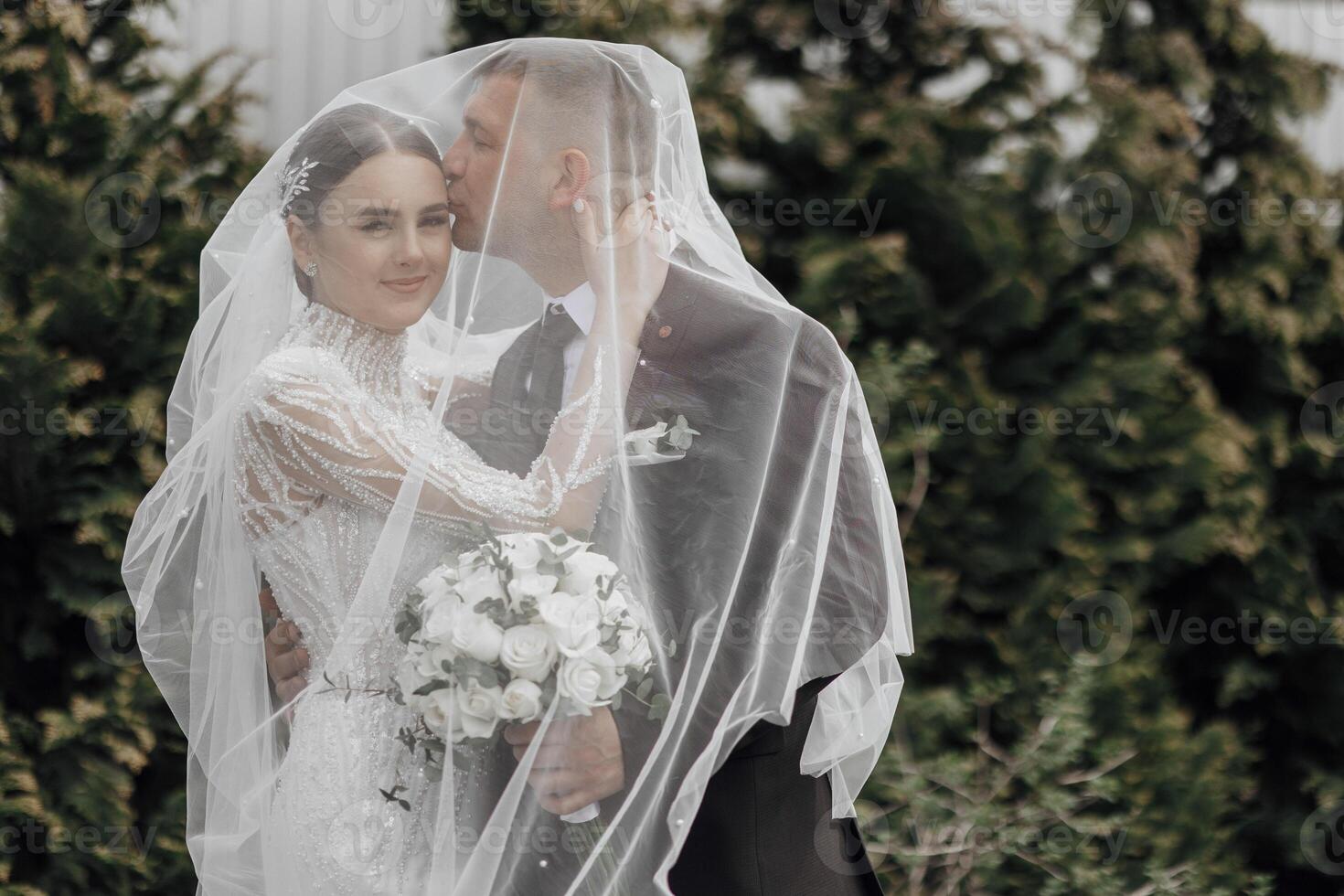 The bride in an elegant dress with a bouquet and the groom in a classic suit are walking in the garden, holding hands. photo