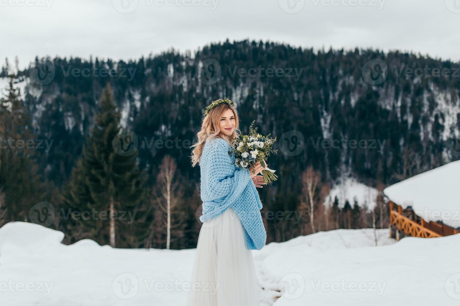 retrato de un linda novia en un blanco vestir con un ramo de flores de flores en su manos, envuelto en un azul tartán, esperando para el novio en contra el antecedentes de un invierno paisaje de nevadas montañas. foto