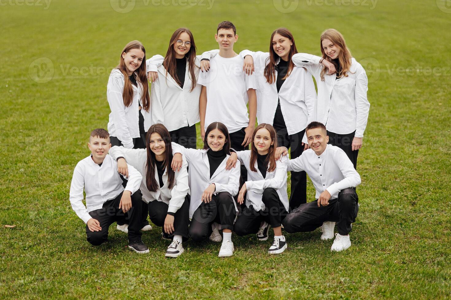 A group of many happy teenagers dressed in the same outfit having fun and posing in a stadium near a college. Concept of friendship, moments of happiness. School friendship photo