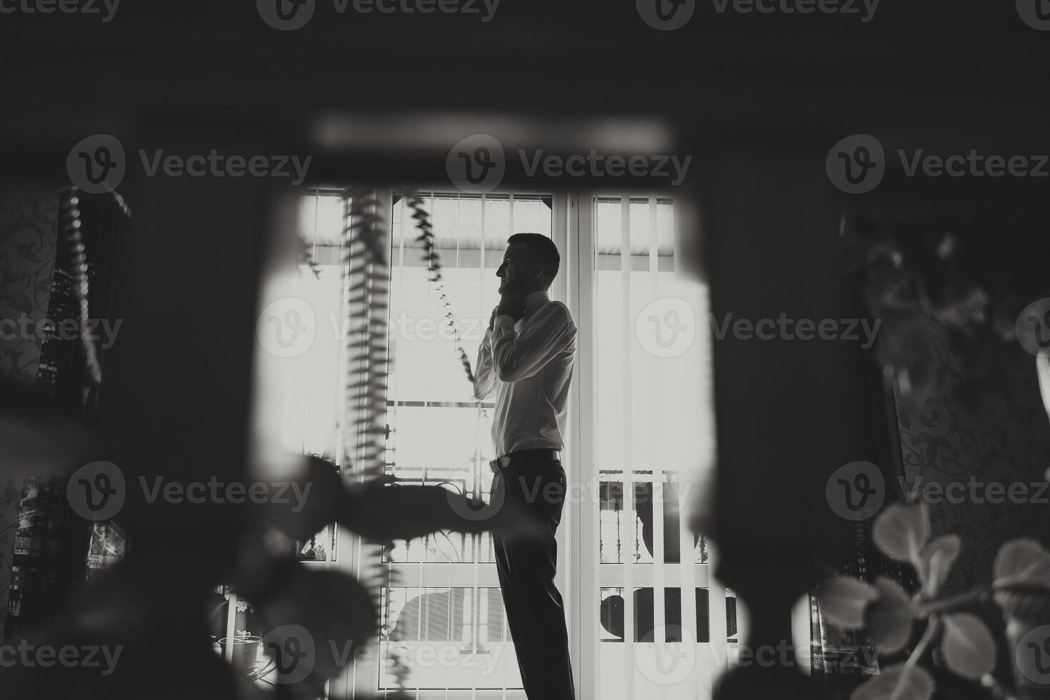 A stylish groom is tying his tie in preparation for the wedding ceremony. Groom's morning. A businessman wears a tie. Black and white photo in profile.