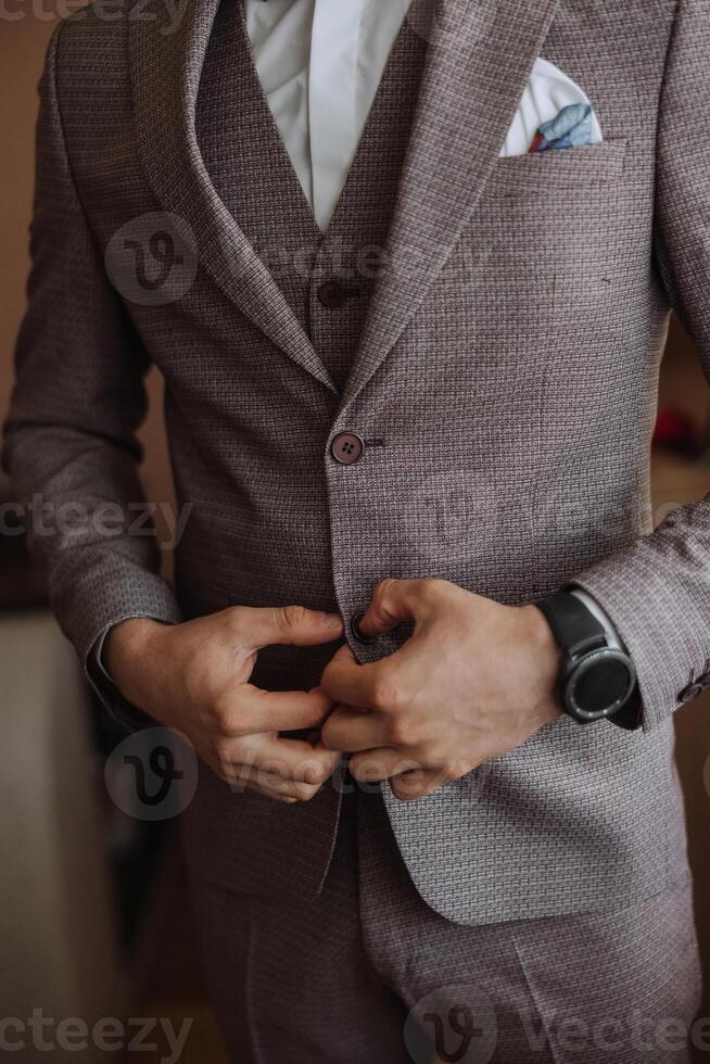 el hombre sujeta el botones en su chaqueta. el novio es preparando para el Boda ceremonia. detallado de cerca foto de manos