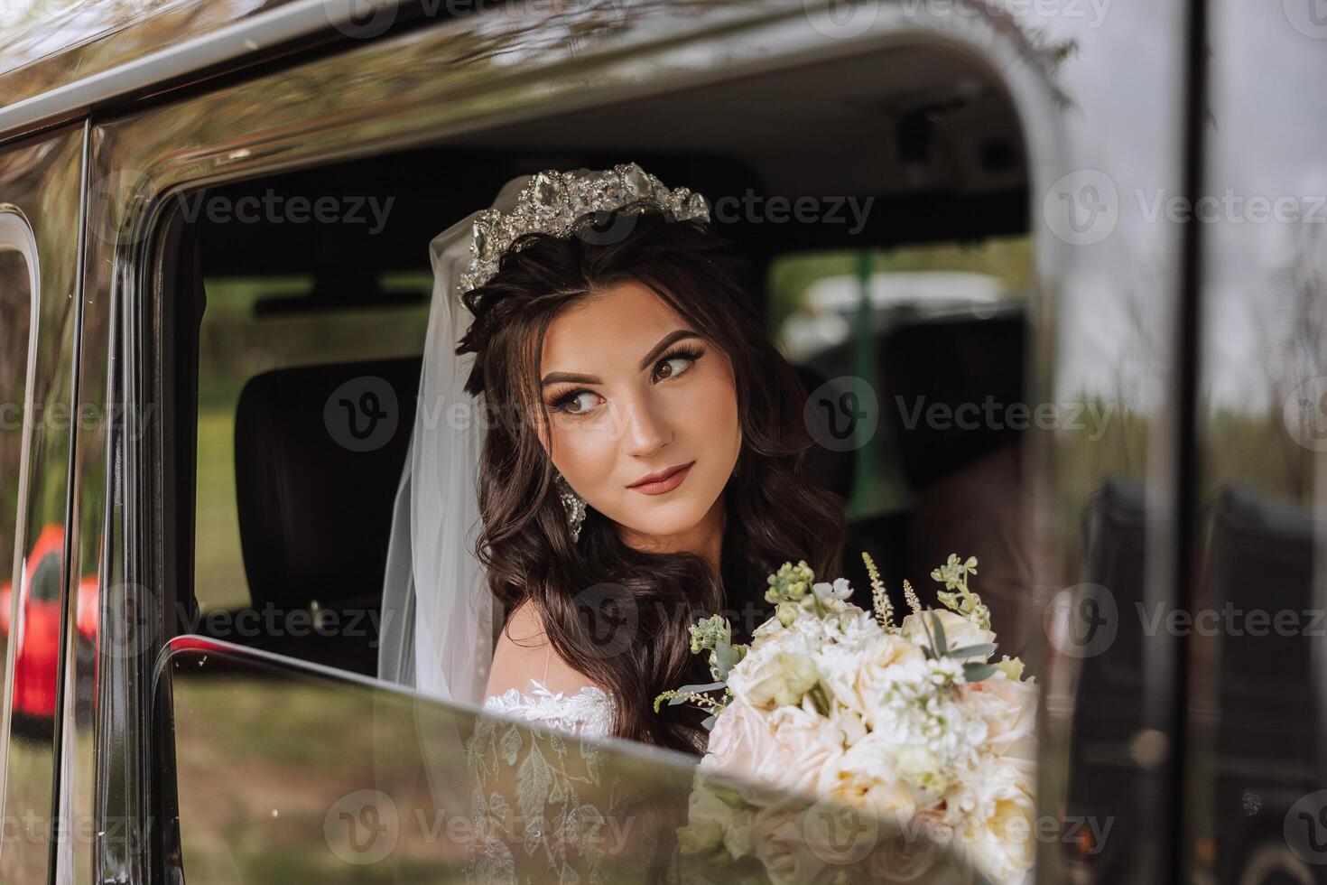 A beautiful bride, sitting in a car, looks out of the open window of the car. A beautiful bride with a bouquet of flowers in her hands is sitting in a stylish expensive car. photo