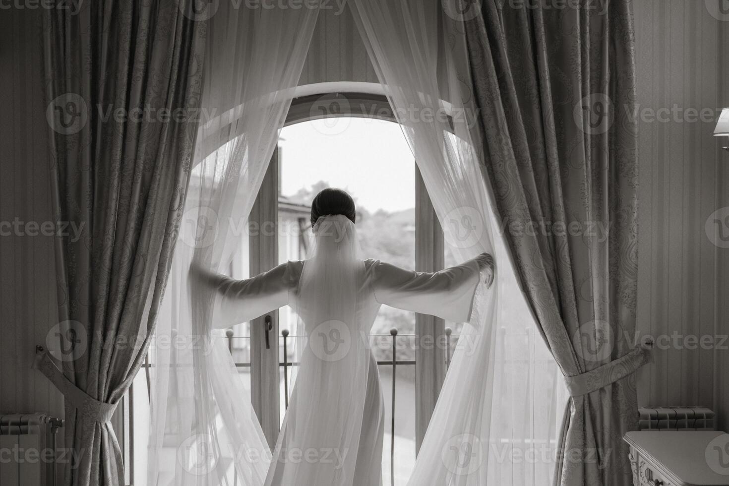 Rear view of woman standing near window of modern luxury apartment or hotel room. Black and white photo