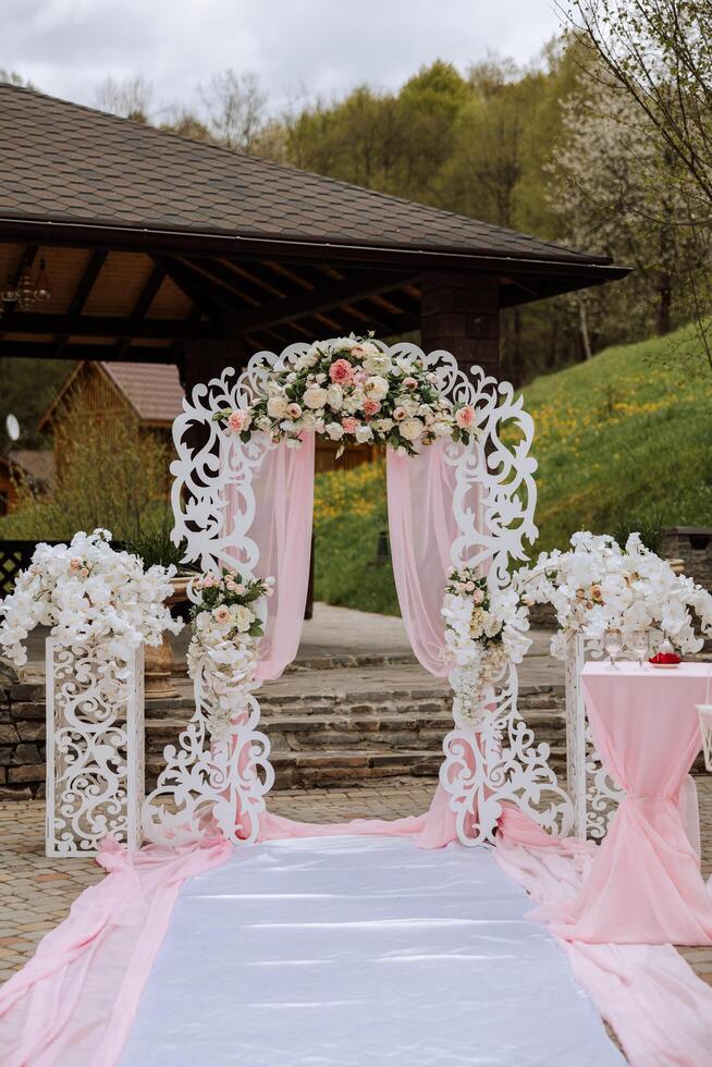 Boda decoración. blanco pista. un blanco y rosado arco decorado con flores preparación para el Boda ceremonia. celebracion foto