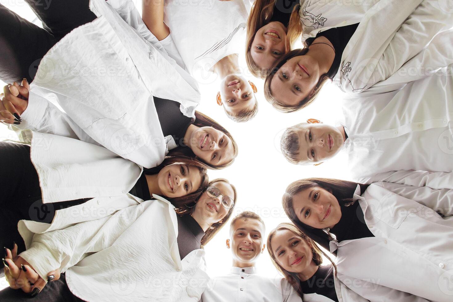 Large group of smiling young people standing, hugging, looking at camera. Group of cheerful teenage people in a circle looking down. Low viewing angle. Copy space. photo