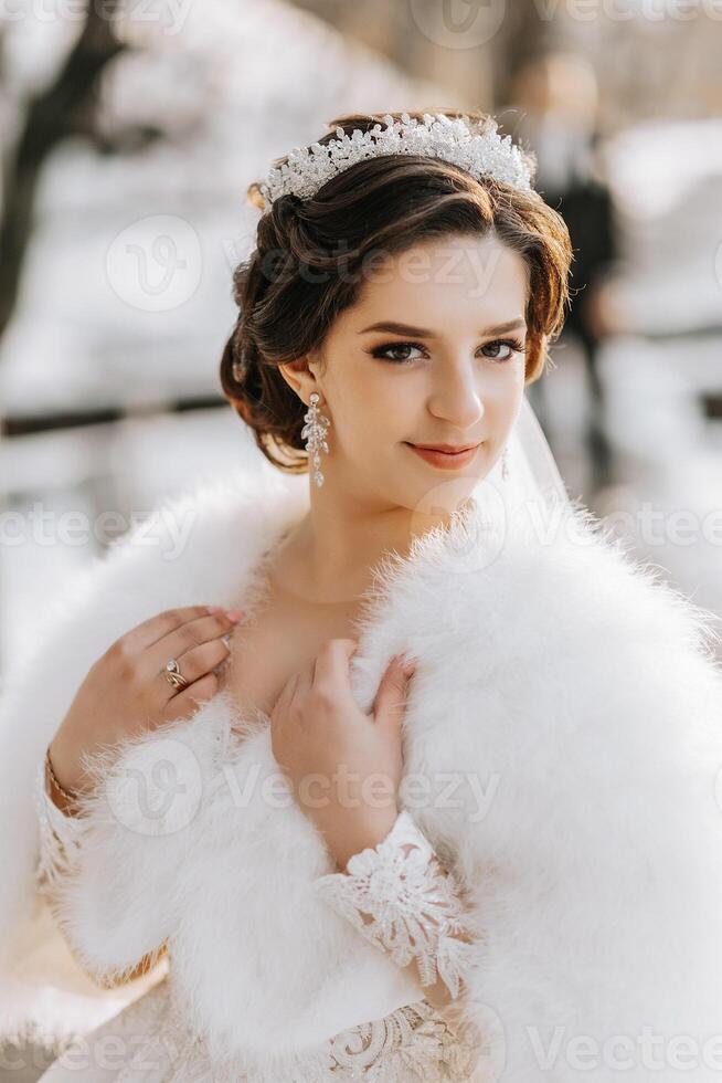 Portrait of a beautiful bride with a wedding bouquet of flowers, attractive woman in a wedding dress with a long veil. Happy bride woman. Bride with wedding makeup and hairdo. Winter wedding photo