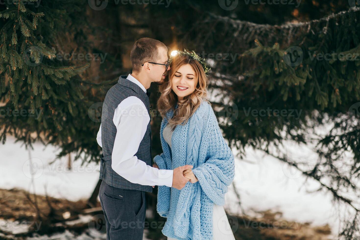 Happy and smiling bride and groom on the background of winter forest. A handsome groom tenderly holds the hands of his bride and kisses her. The concept of a modern winter wedding. photo