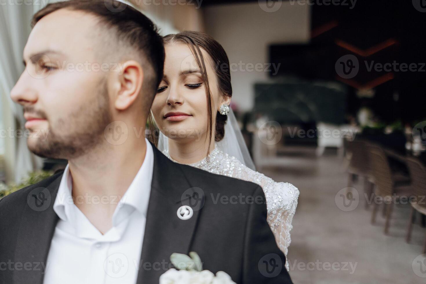 Lovely newlyweds. The bride hugs the groom from behind by the shoulders. Portrait of the bride and groom in a lace dress. photo