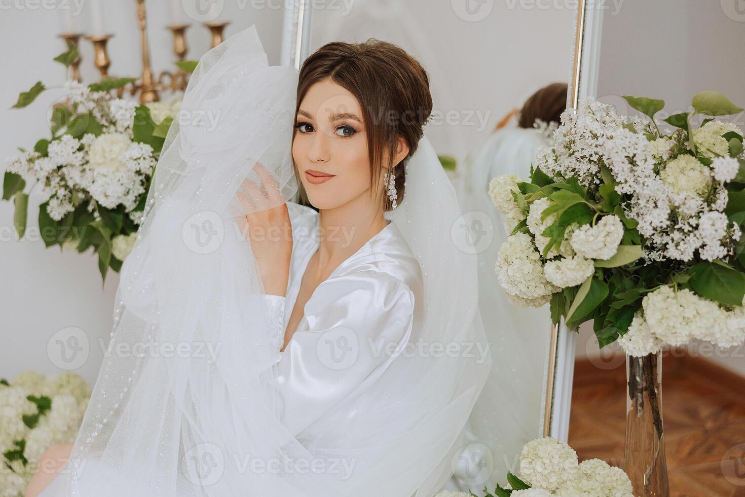 A beautiful brunette bride with a tiara in her hair is getting ready for the wedding in a beautiful robe in boudoir style. Close-up wedding portrait, photo. photo