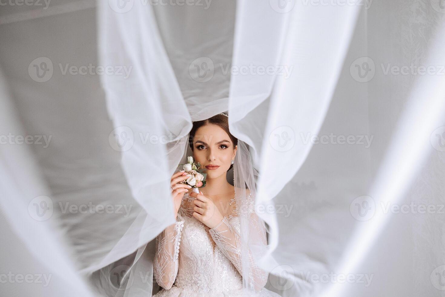 A luxurious bride with a beautiful hairstyle and a gorgeous dress is getting ready for the wedding ceremony in the morning. Morning photo of the bride at home or in a hotel room. Professional makeup.