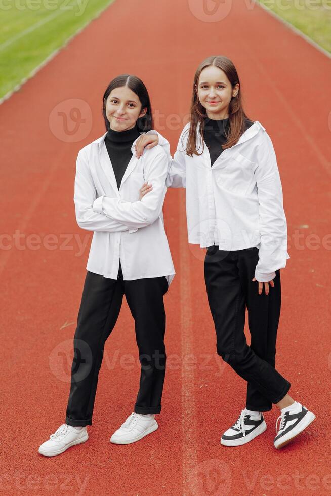 Portrait of two teenage girls in casual clothes sitting in a stadium and posing looking at the camera. Concept of friendship. A moment of happiness. photo