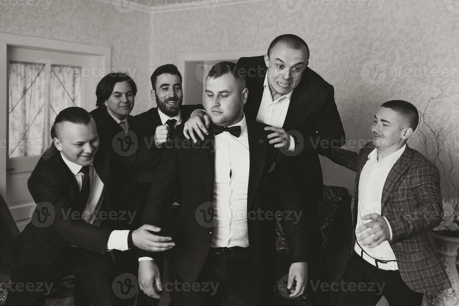 A young groom and his funny friends pose for the camera. A group of young people hug the groom and cheerfully congratulate him. Happy friends. Friends in the room. Wedding day. Black and white photo. photo