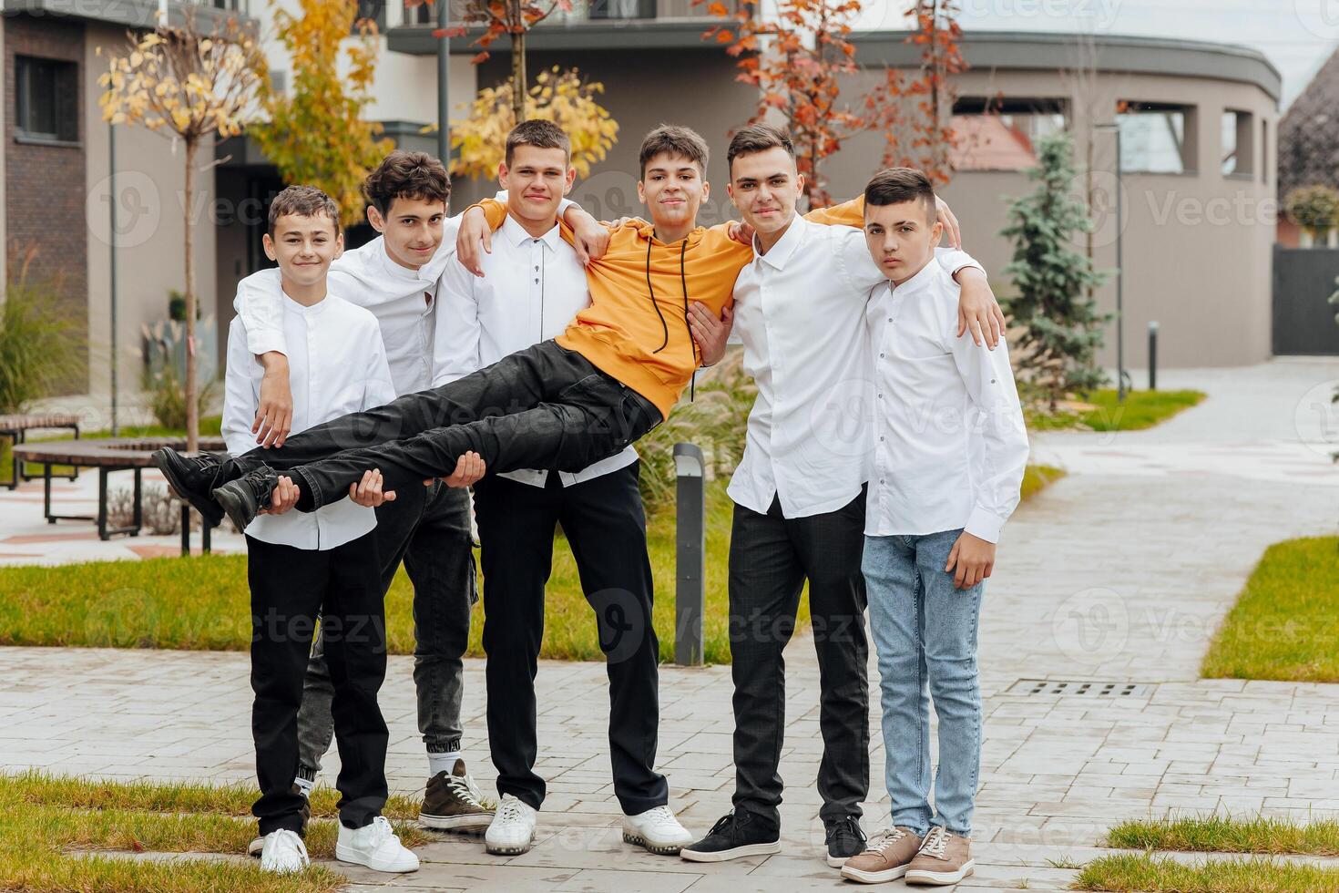 Group of smiling and happy teenage friends wearing casual clothes spending time together, posing and talking with each other near college building on autumn day. photo
