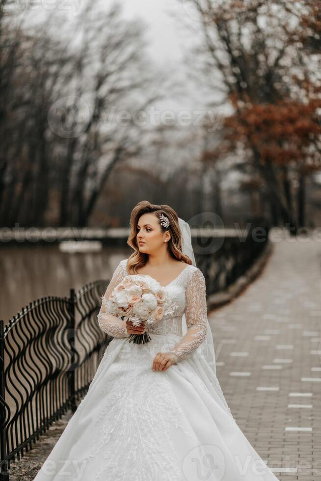 Portrait of a beautiful bride with a wedding bouquet of flowers, attractive woman in a wedding dress with a long veil. Happy bride woman. Bride with wedding makeup and hairdo. Winter wedding photo