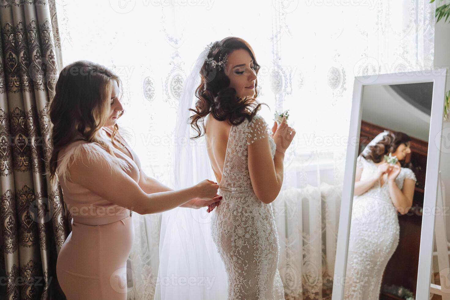 Morning of the bride. The bride's maid of honor helps the bride lace up her dress, fasten buttons on the dress or sleeves. Girlfriends help the bride fasten her dress photo