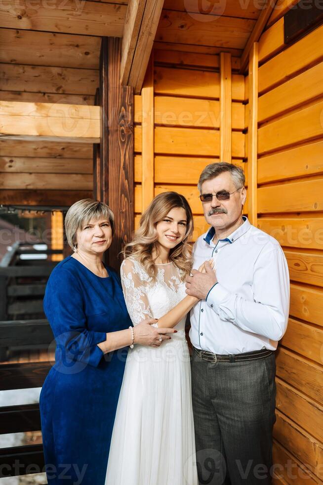 Happy parents rejoice for their daughter, who will soon get married. Touching moments at the wedding. Mom and dad hug daughter bride. Portrait of parents with bride photo