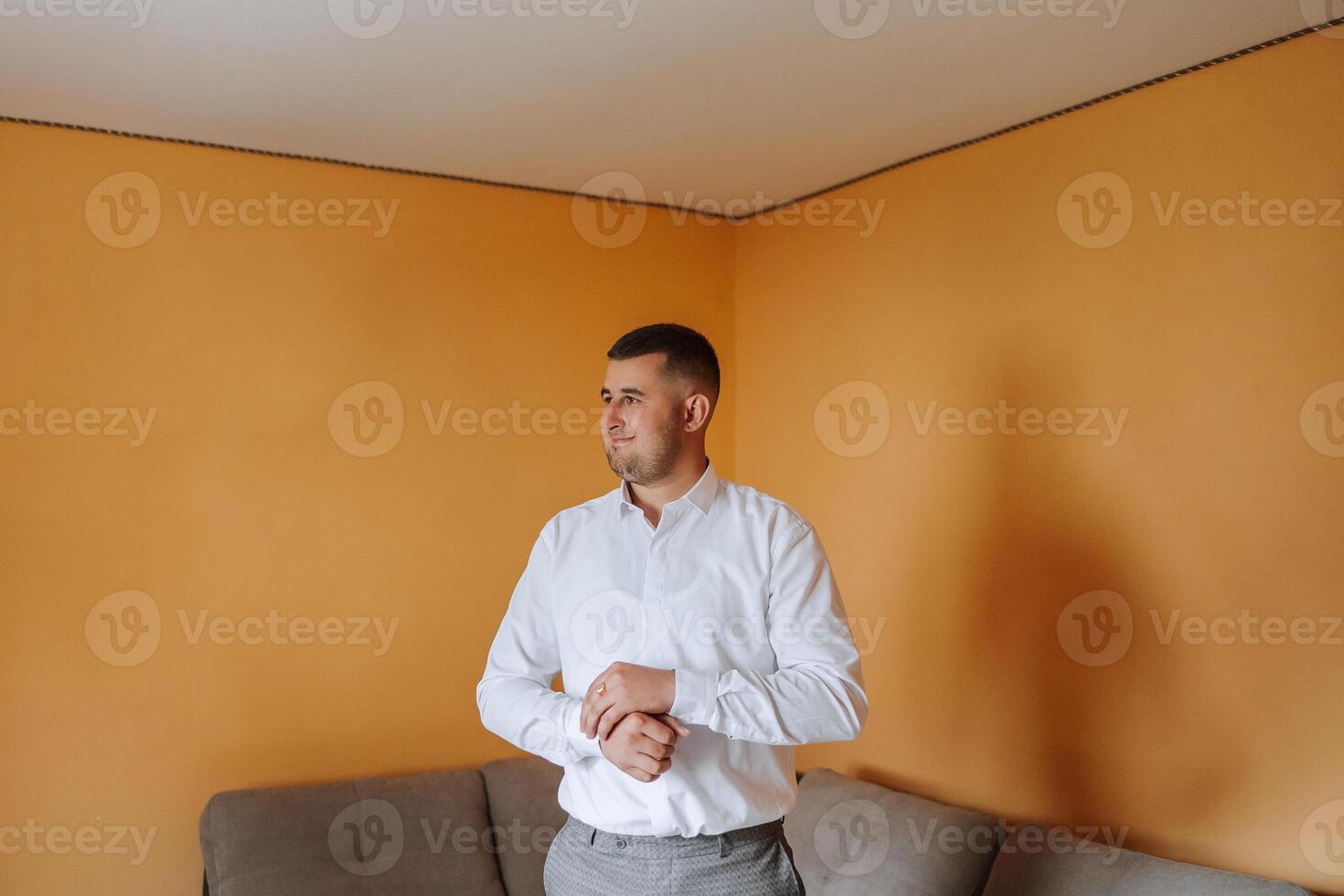 The groom buttons his shirt by the window. man in a shirt. Male portrait. Photoshoot at the window. Groom's collection. Wedding day. Handsome man groom buttoning his shirt in a hotel room. photo