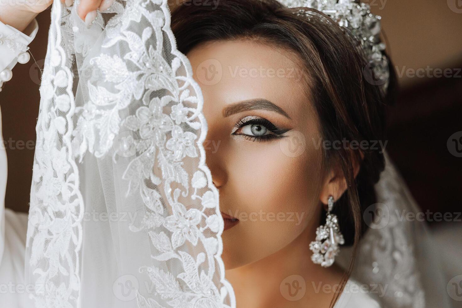 A beautiful brunette bride with a tiara in her hair is getting ready for the wedding in a beautiful robe in boudoir style. Close-up wedding portrait, photo. photo