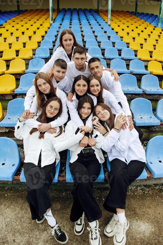 un grupo de muchos contento adolescentes vestido en el mismo atuendo teniendo divertido y posando en un estadio cerca un colega. concepto de amistad, momentos de felicidad. colegio amistad foto