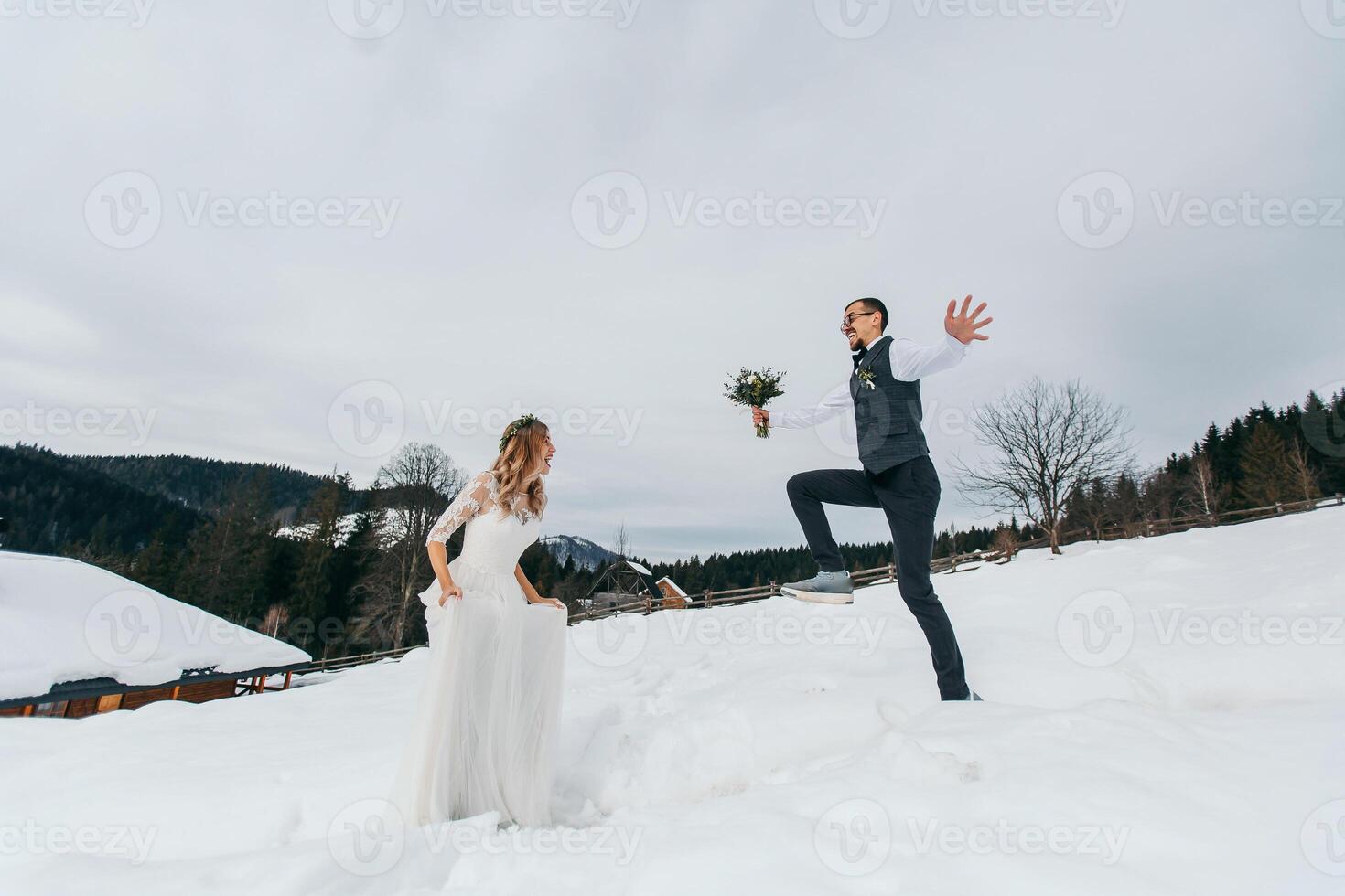 Young couple bride and groom playing in winter nature against the background of snowy mountains. To play snowballs. Jump. Have a good time laughing. photo