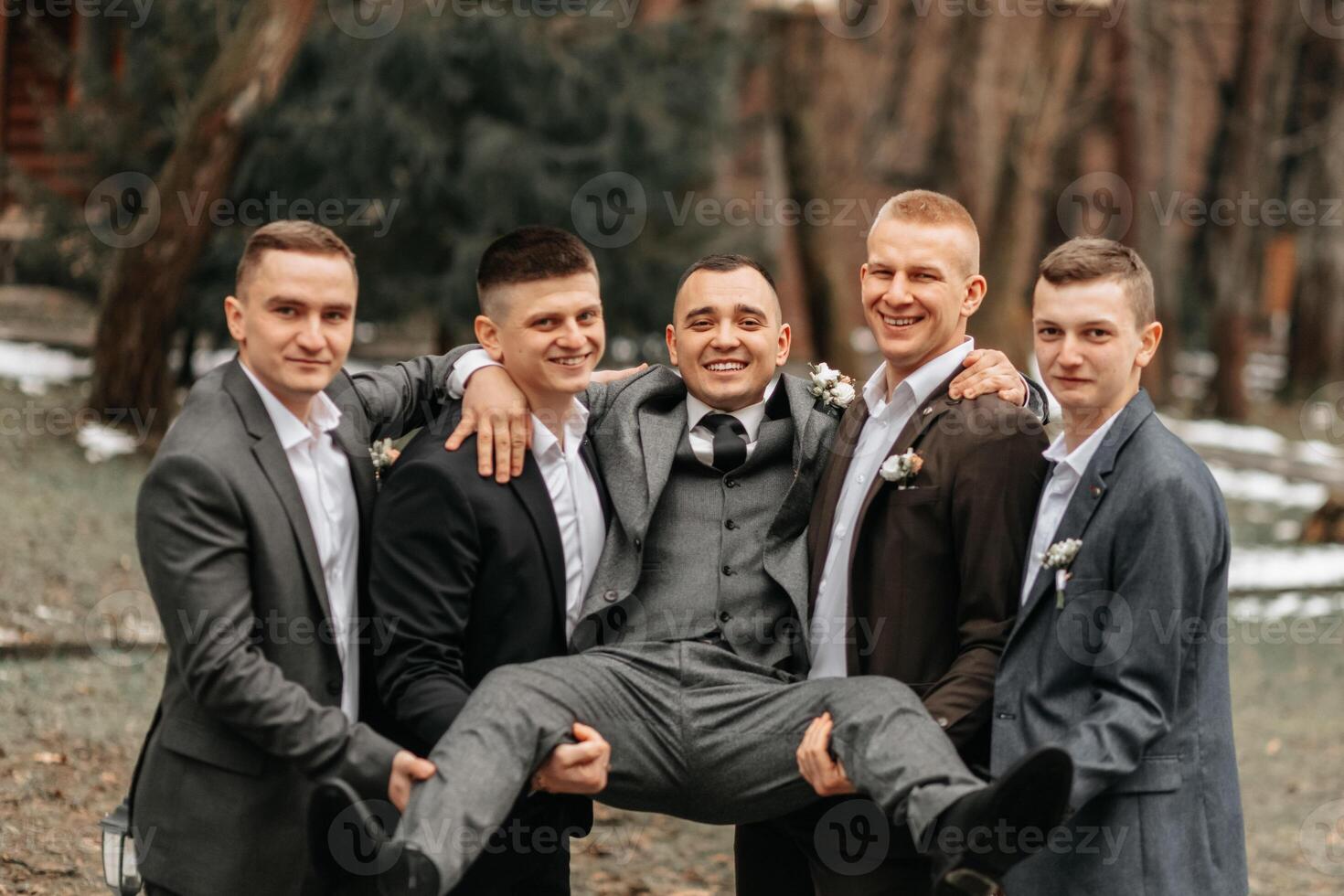 The groom and his friends are dressed in suits, fooling around in nature during a photo shoot. A group of men. Wedding in nature