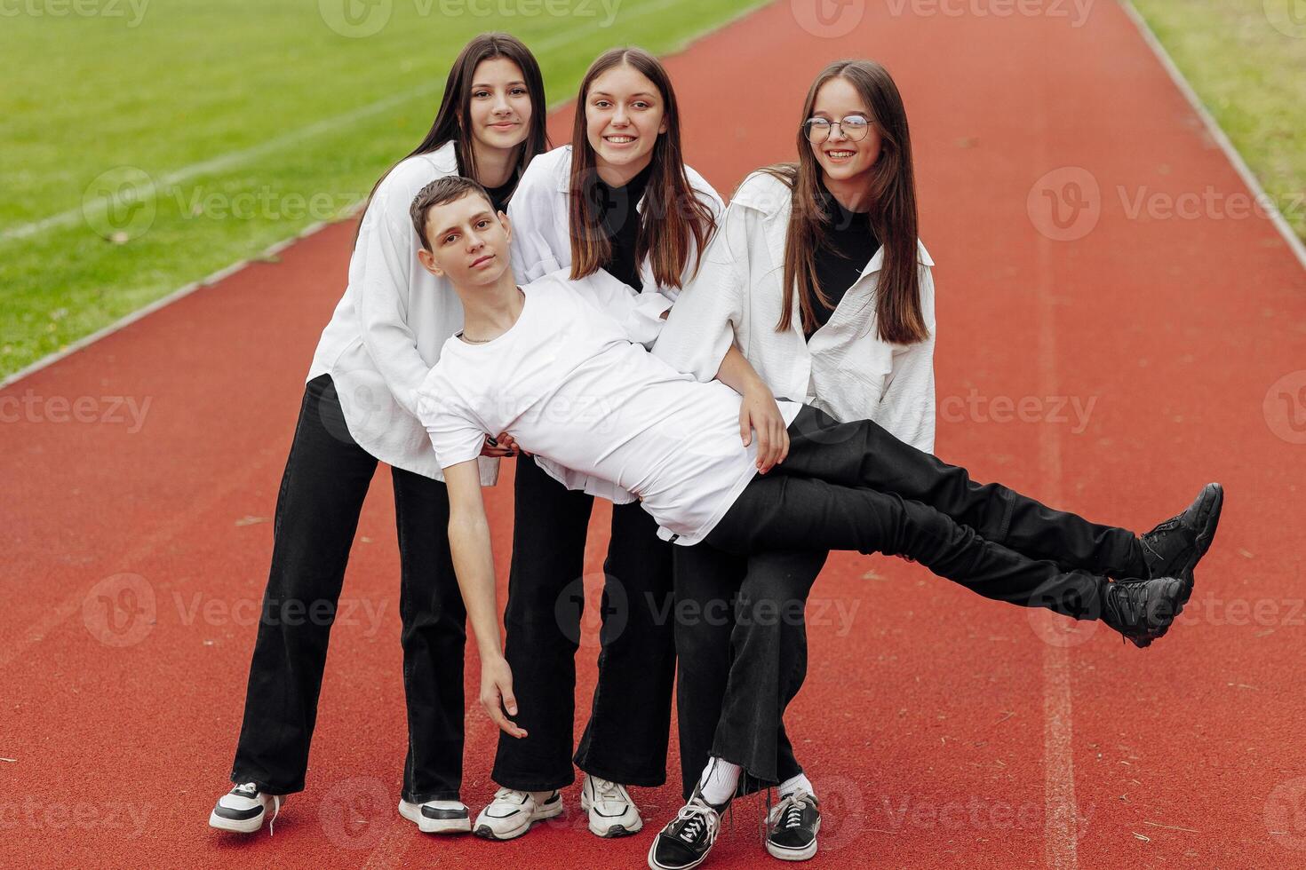 Portrait of four teenage in casual clothes sitting in a stadium and posing looking at the camera. Concept of friendship. A moment of happiness. photo