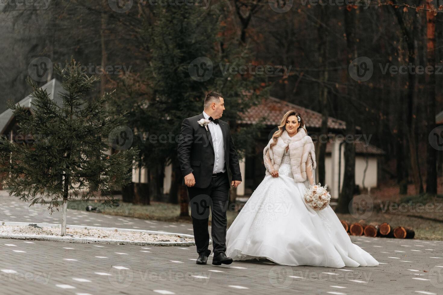 The bride and groom are walking near the hotel and posing, happy and enjoying the day, holding hands. A long train on the dress. Winter wedding photo