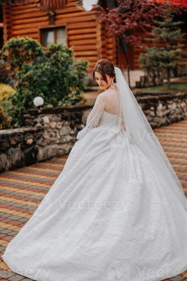 un Pelirrojo novia en un elegante vestir con largo mangas y un hermosa ornamento en su cabello, poses con su espalda convertido a el cámara. largo tren de el vestido. foto