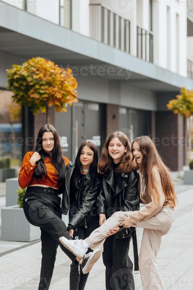 Group of smiling and happy teenage friends wearing casual clothes spending time together, posing and talking with each other near college building on autumn day. photo