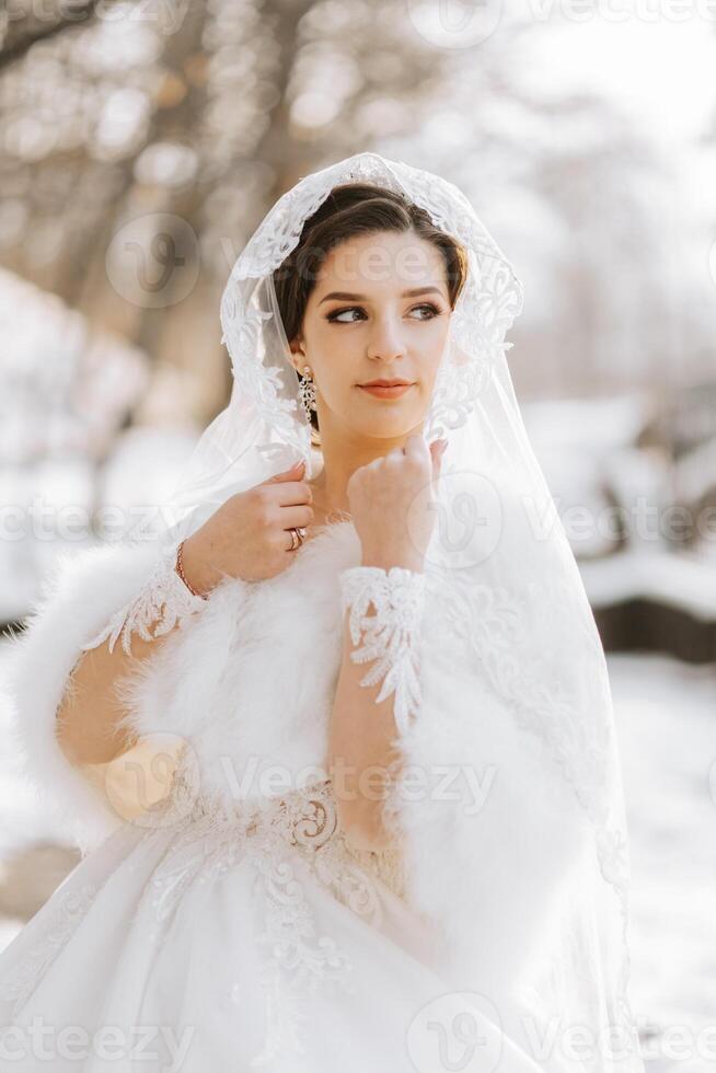 Portrait of a beautiful bride with a wedding bouquet of flowers, attractive woman in a wedding dress with a long veil. Happy bride woman. Bride with wedding makeup and hairdo. Winter wedding photo