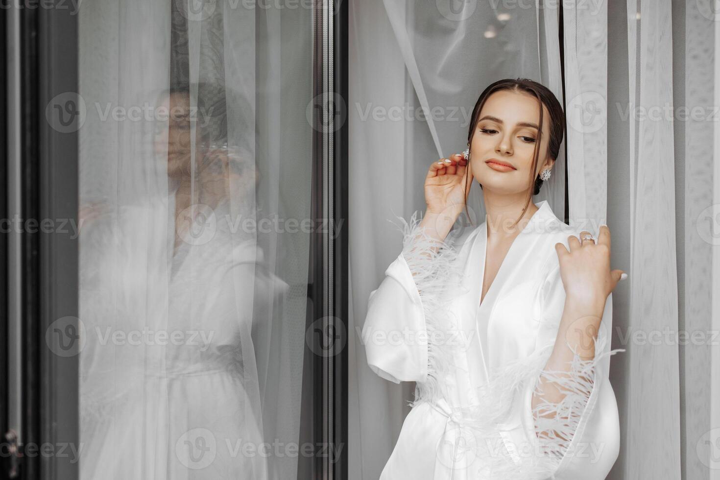 portrait of bride girl in white gown with professional hairstyle and natural makeup in hotel room with reflection in window. The best day photo