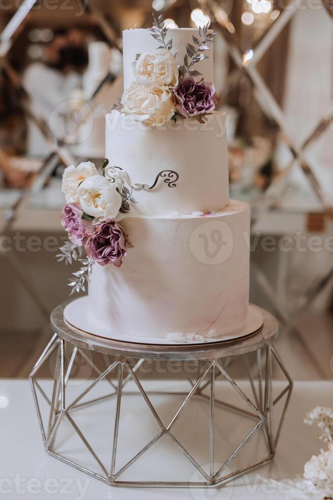 A large luxurious tiered wedding cake decorated with fresh rose flowers in the banquet hall. Wedding dessert under the evening light. Wedding decor. photo