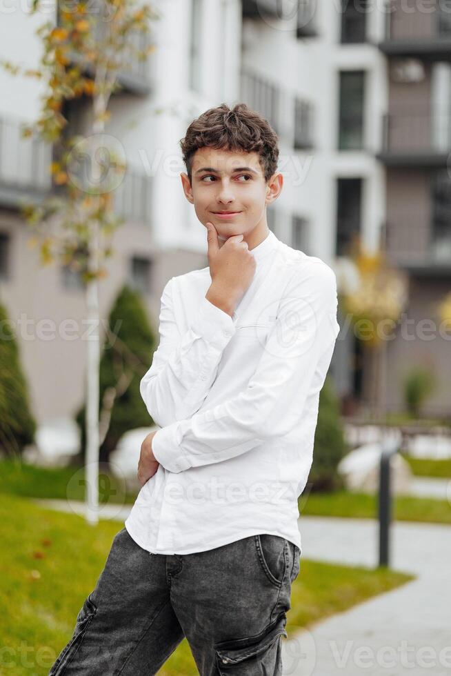 Vertical close-up portrait of a teenager in casual clothes. Happy smiling teenager in autumn park in sunlight. A beautiful child looks at the camera in nature. photo