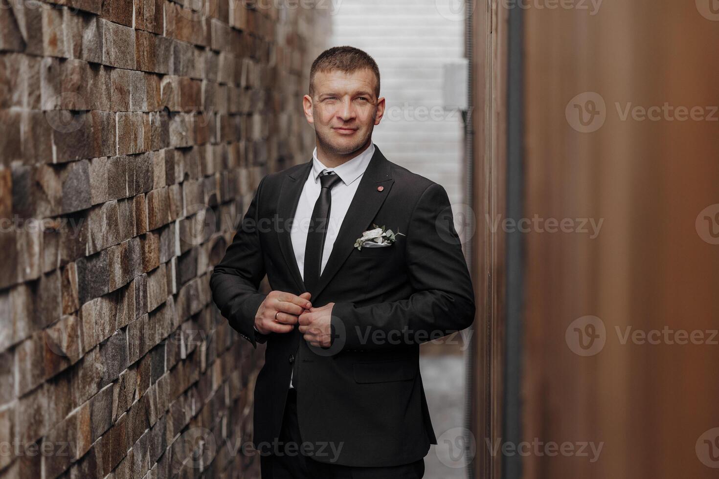 A man poses in a suit near a stone wall. Business style. Groom in a suit. photo