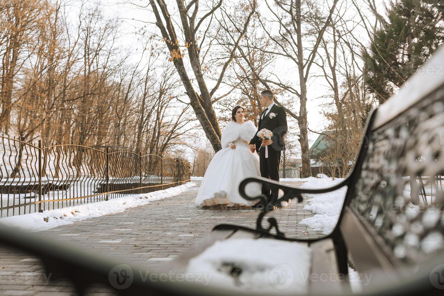 Winter wedding. Happy couple walking in wedding clothes hugging and smiling in a winter park covered with snow on their wedding day. Winter love story of a beautiful couple in snowy winter weather photo