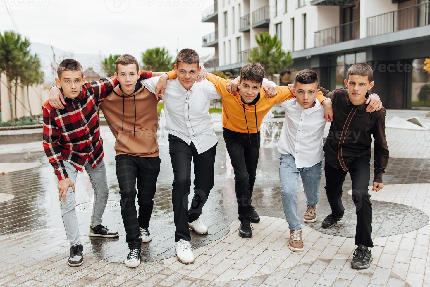 Group of smiling and happy teenage friends wearing casual clothes spending time together, posing and talking with each other near college building on autumn day. photo