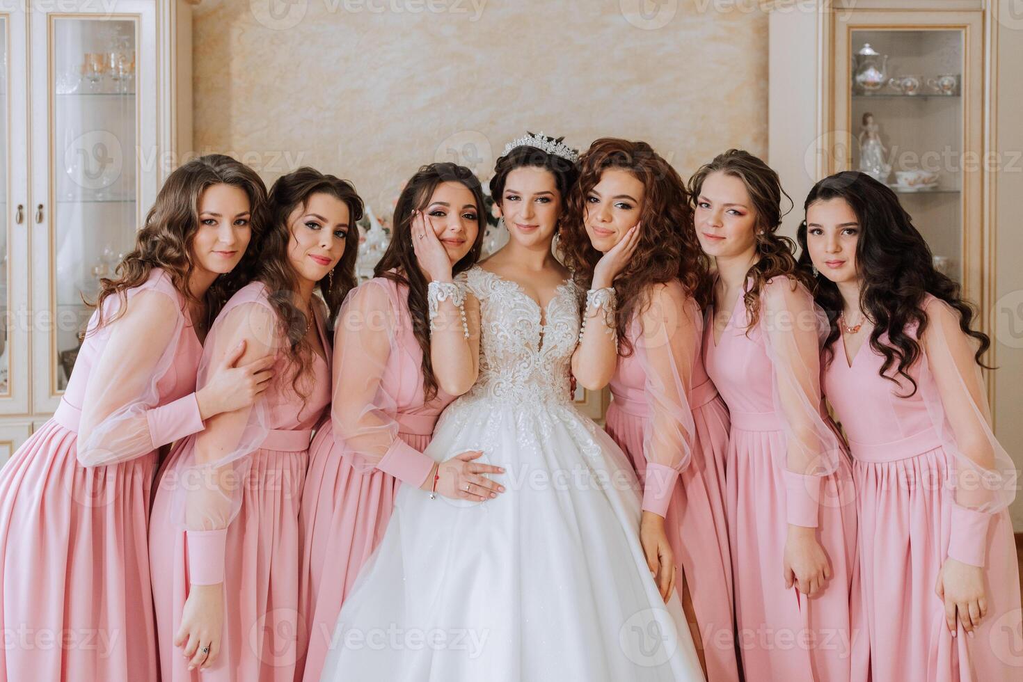 retrato de el novia con su amigos en el habitación. un morena novia en un largo blanco vestir y su amigos en rosado vestidos son sonriente y contento. joven chicas. foto