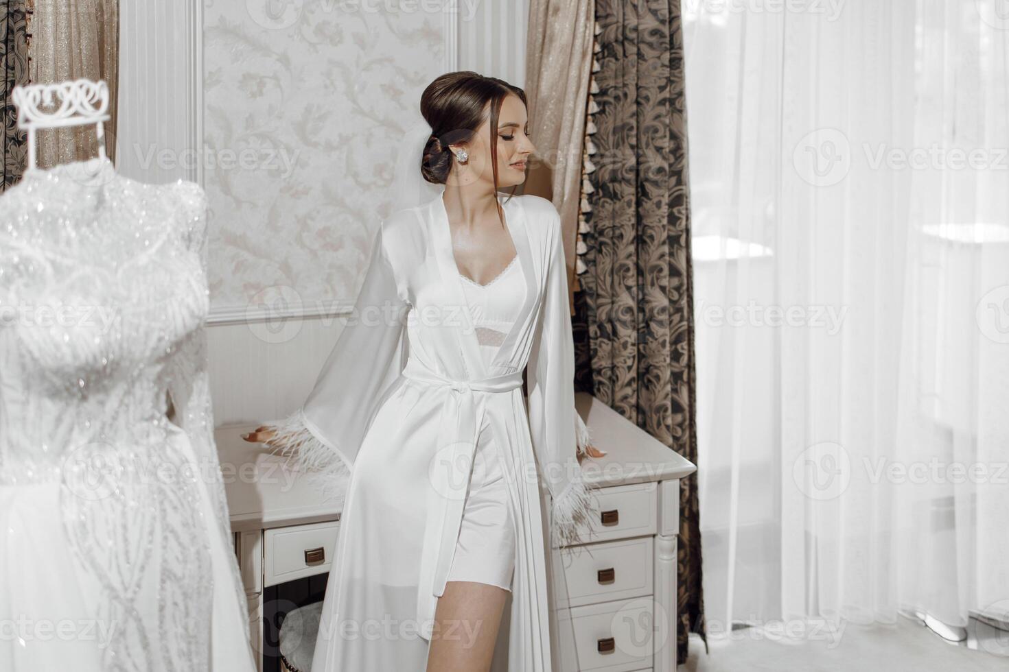 retrato de novia niña en blanco túnica con profesional peinado y natural maquillaje en hotel habitación con maravilloso interior. Boda vestir con mangas en un maniquí foto