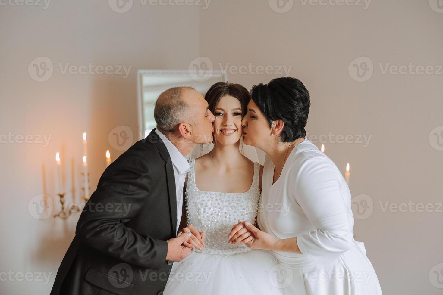 Happy parents hold the hands of the bride who is getting married and support her, wearing a wedding dress and a long veil. photo