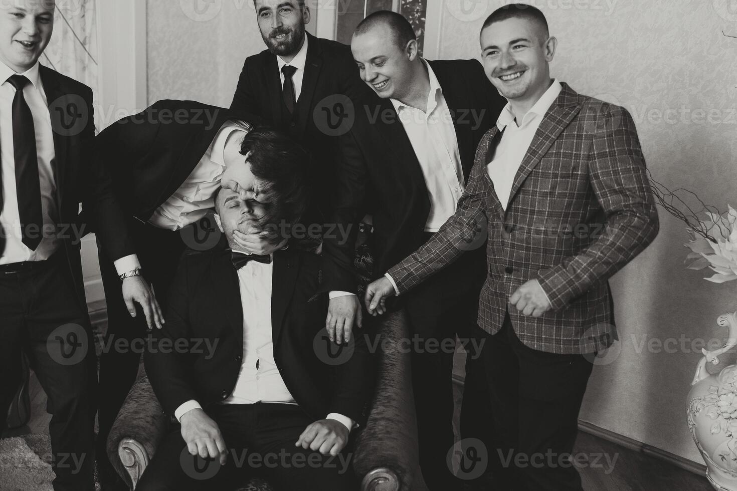 un joven novio y su gracioso amigos actitud para el cámara. un grupo de joven personas abrazo el novio y alegremente felicitar a él. contento amigos. amigos en el habitación. Boda día. negro y blanco foto. foto