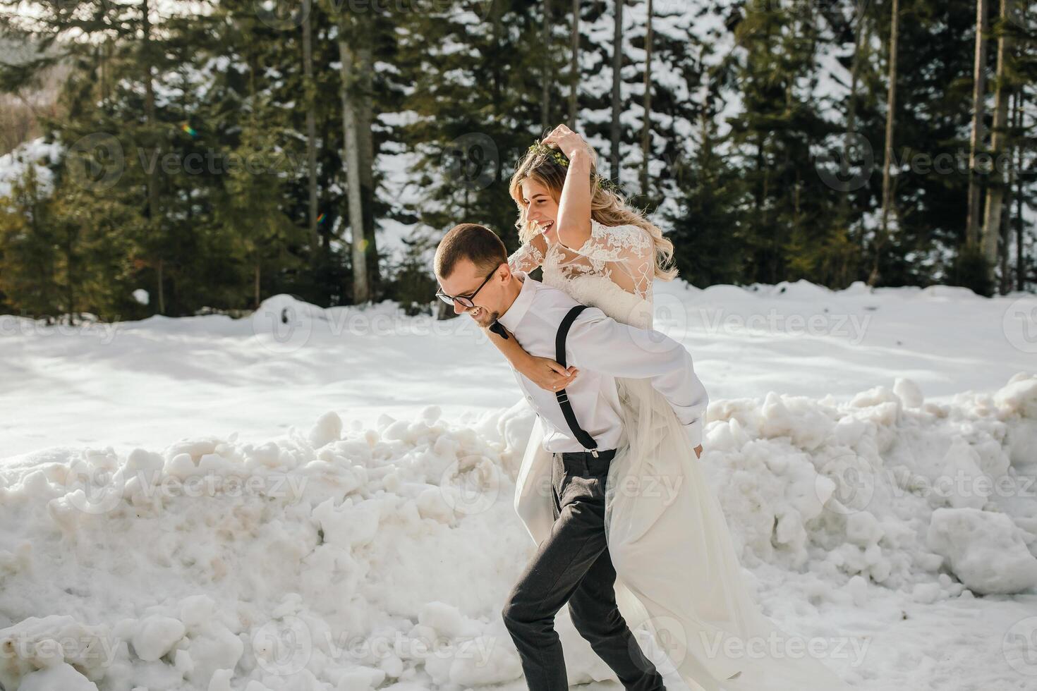 el novia y novio son corriendo a lo largo un Nevado la carretera en contra el antecedentes de un pino bosque y hermosa contraste luz de sol. lado vista. invierno boda. sitio para logo. foto