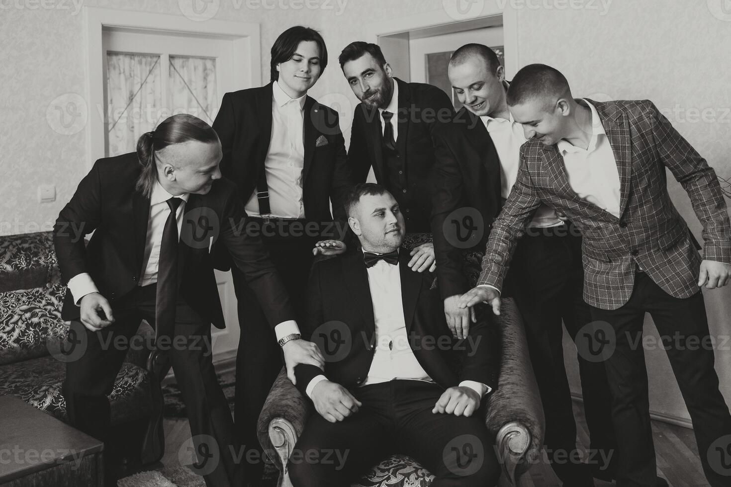 A young groom and his funny friends pose for the camera. A group of young people hug the groom and cheerfully congratulate him. Happy friends. Friends in the room. Wedding day. Black and white photo. photo