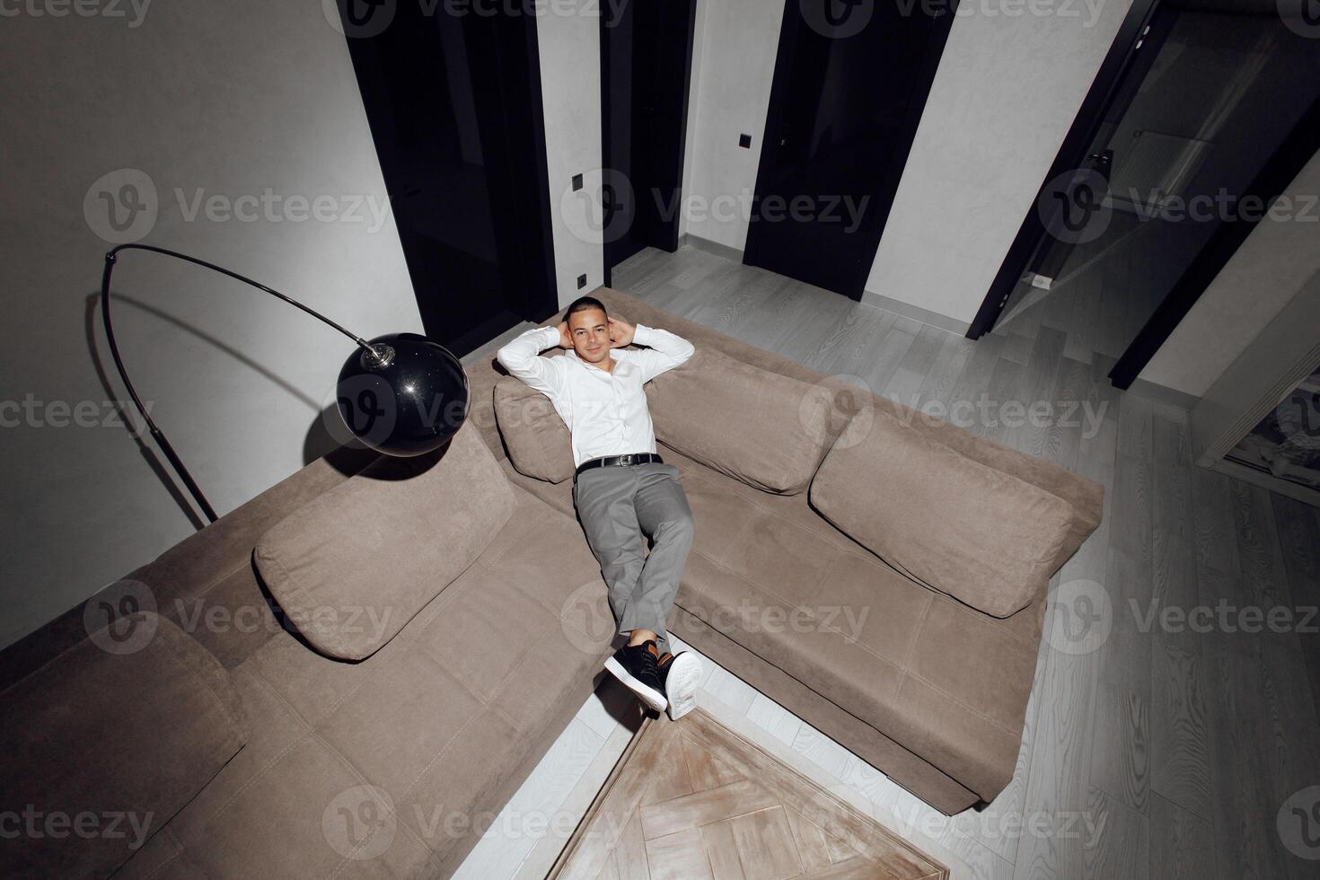 Satisfied handsome guy relaxing on sofa in hotel, resting, looking at camera, hands behind head, smiling happily. Relaxation, self care, enjoy life concept photo