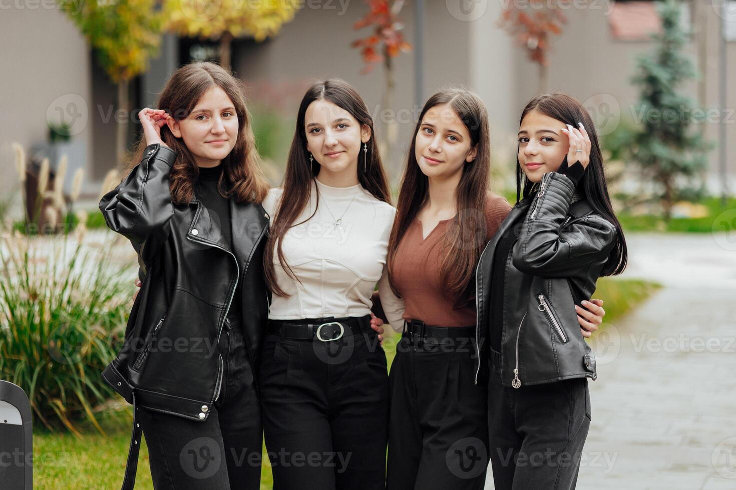 Group of smiling and happy teenage friends wearing casual clothes spending time together, posing and talking with each other near college building on autumn day. photo
