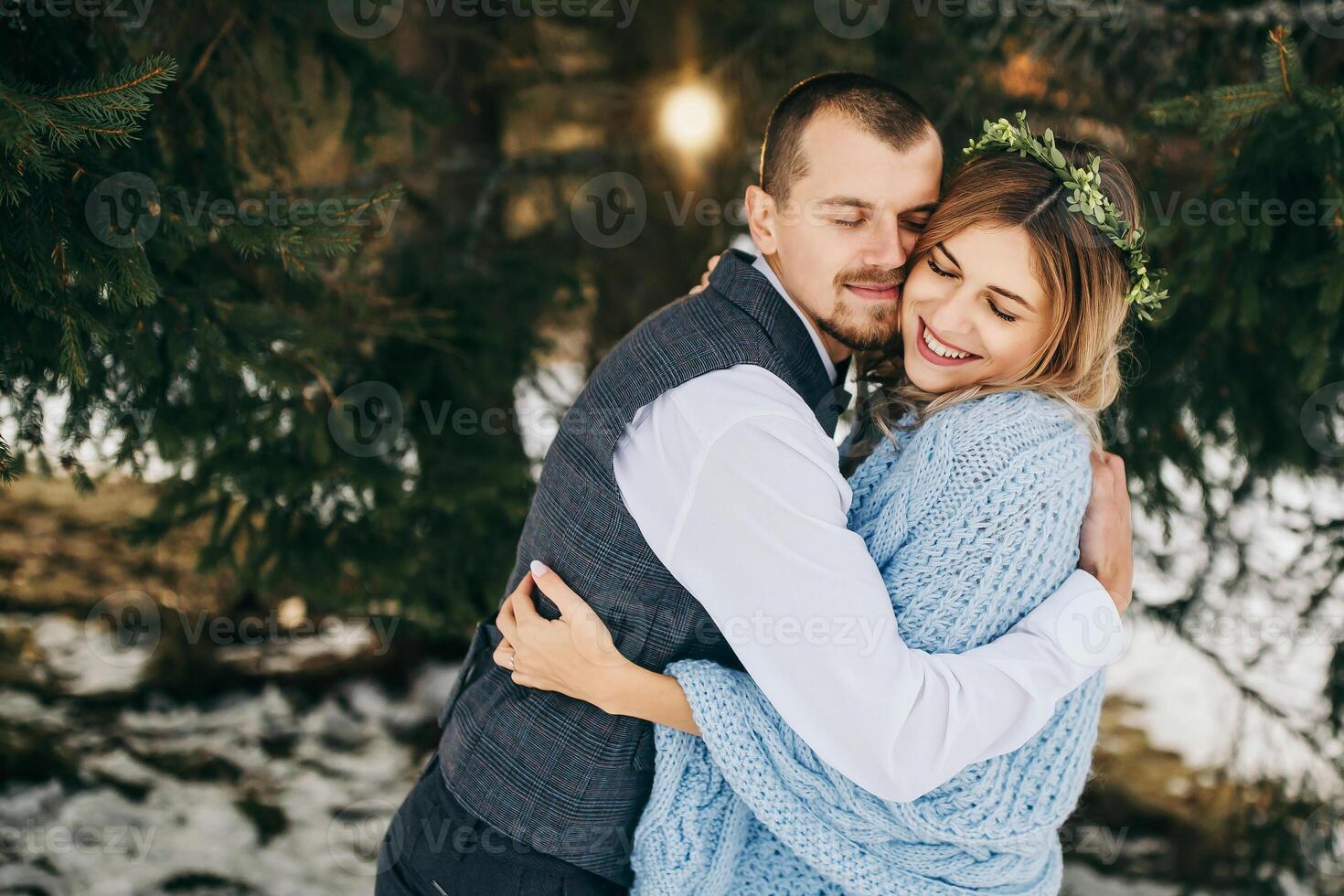 Happy and smiling bride and groom on the background of winter forest. A handsome groom tenderly hugs his bride. The concept of a modern winter wedding. photo