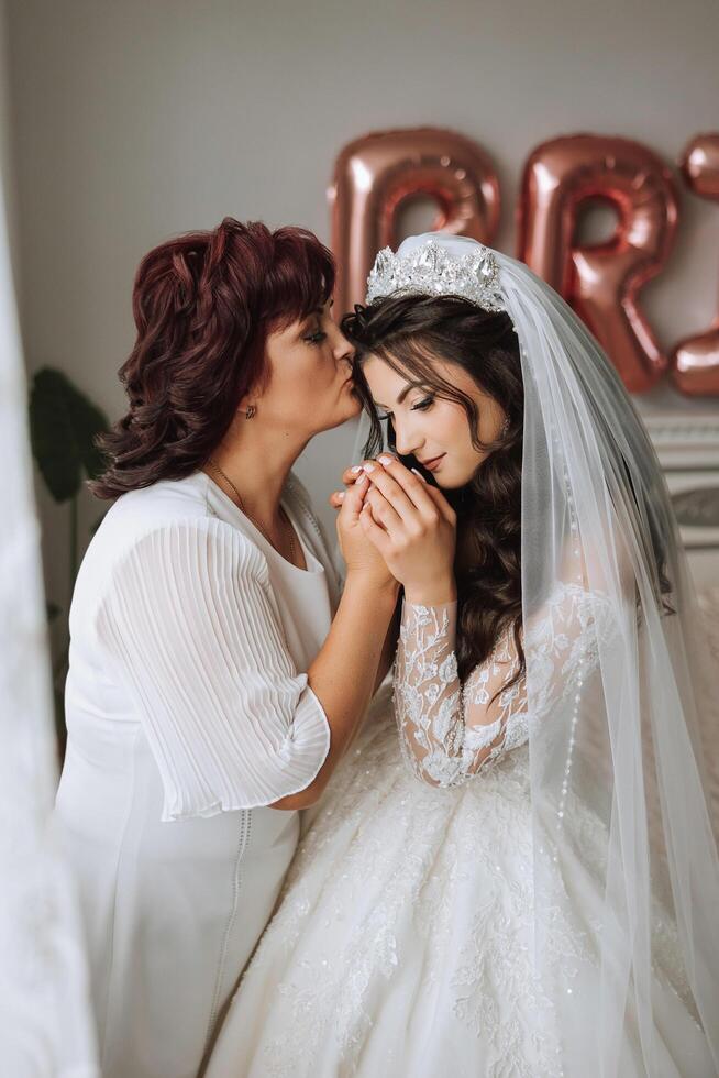 A beautiful and happy mother and her daughter, the bride, are standing next to each other. The best day for parents. Tender moments at the wedding. photo