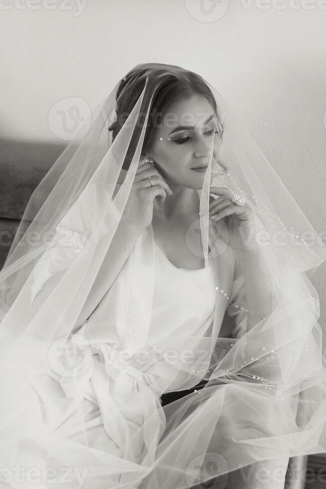 A beautiful brunette bride with a tiara in her hair is getting ready for the wedding in a beautiful robe in boudoir style. Close-up wedding portrait, photo. photo