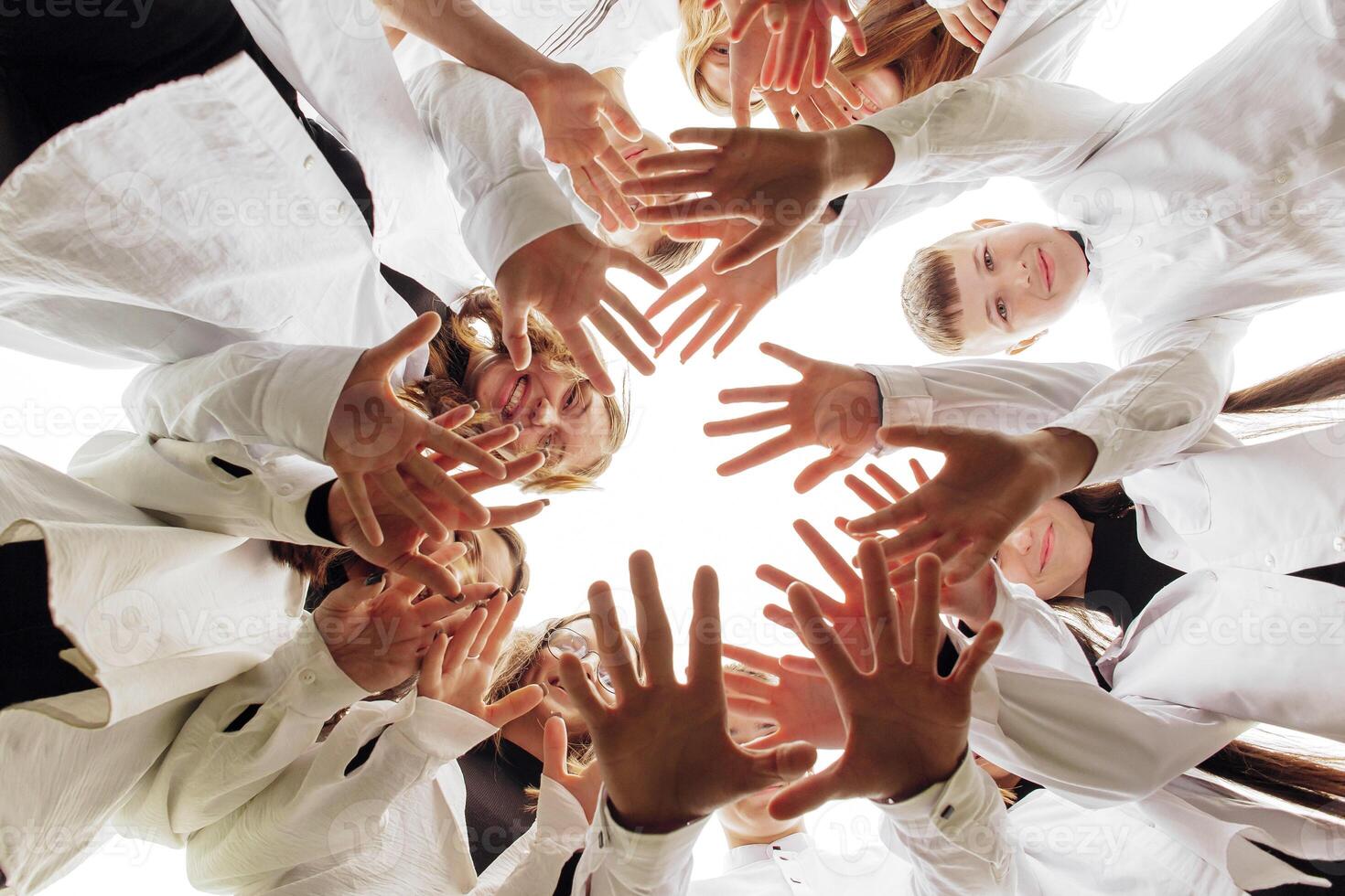 A large group of smiling young people standing, hugging, looking at the camera and stretching their arms down. Group of cheerful teenage people in a circle looking down. Low viewing angle. Copy space. photo